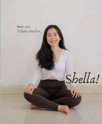 Shella duduk bersila tersenyum, instruktur pilates